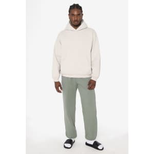 A model wears a light grey hoodie with green fleece sweatpants and black sandals, standing against a plain background.