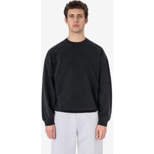 A black garment dye heavy fleece pullover worn by a model, styled with grey trousers. It features a logo.