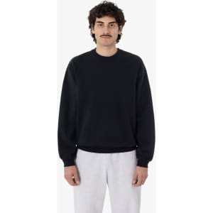 A man wearing a black garment dye heavy fleece pullover, paired with light grey sweatpants. The pullover features a logo.