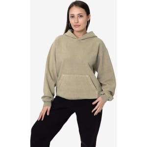 A hooded pullover in beige fleece, featuring a front pocket and a relaxed fit. The model poses against a plain backdrop.