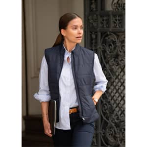 A navy women's vest is worn over a light blue shirt, paired with dark pants and a belt. A logo is visible on the vest.