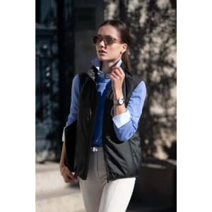 A woman wearing a black unisex vest over a blue shirt, styled with sunglasses and light-coloured trousers.