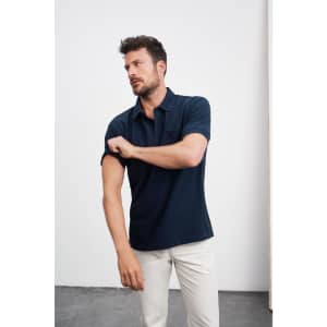 A navy polo shirt with a short sleeve, featuring a pocket and a brand logo. Model adjusts the sleeve.