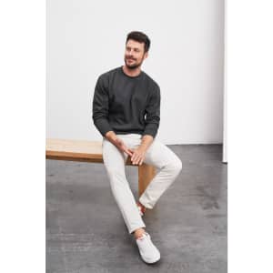 A round-neck heavy sweater in dark grey worn by a man seated on a wooden bench, paired with light trousers.