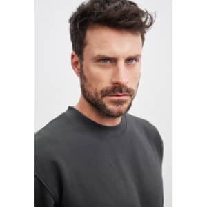 A model wearing a dark grey round-neck sweater. The sweater features a simple design and relaxed fit.