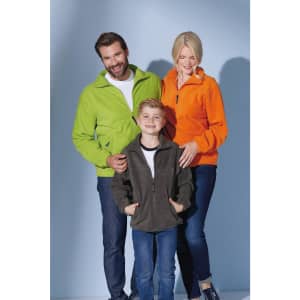 A family wears lightweight polar fleece jackets in green, orange, and dark grey, featuring pockets and zip details.