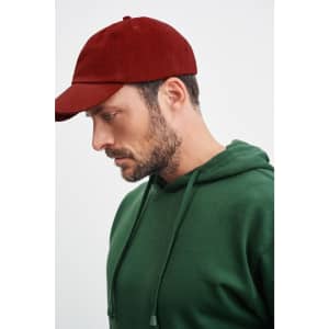A man wearing a green hooded sweatshirt and a maroon cap, facing sideways. The cap has a logo.