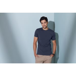 A navy elastic T-shirt is worn by a man standing against a light blue wall. The shirt has a logo.