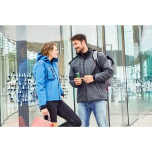 A blue softshell jacket worn by a woman and a grey softshell jacket on a man, both standing outdoors.