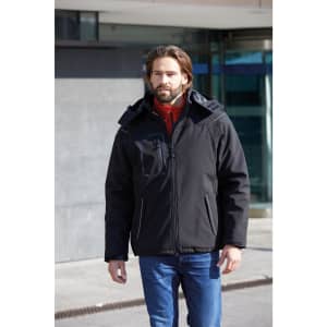 A man in a black softshell jacket with a hood, featuring a zippered pocket, walks outside.
