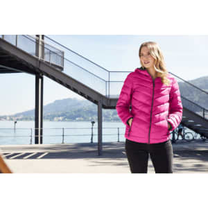 A pink ladies down jacket with a hood, featuring side pockets, worn by a woman outdoors near water.