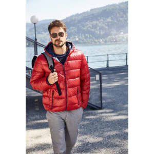 A red men's down puffer jacket with a hood, worn over a navy top, paired with light trousers and sunglasses.