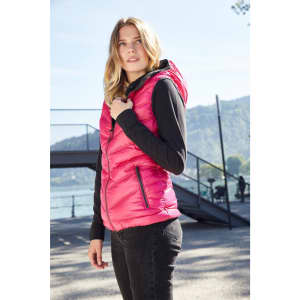 A pink ladies down vest with a hood, featuring zip pockets, displayed outdoors near a lake.