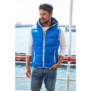 A blue padded men's vest with a hood, worn over a white long-sleeve top and paired with denim shorts.