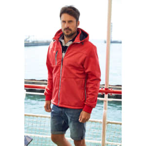 A red men's maritime jacket with a hood, featuring a logo, worn by a man near water.