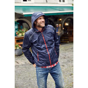 A navy blue men's rain jacket with red accents and a hood, worn by a smiling man outdoors.