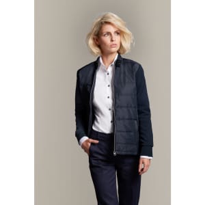 A ladies' hybrid sweat jacket in navy, featuring a zip front, a logo, and a stylish fit paired with a button-up shirt.