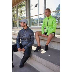 A grey ladies sports softshell jacket and a bright green one, featuring a logo, are modelled by two individuals outdoors.