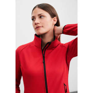 A red ladies softshell jacket with a high collar and a zip front, featuring a logo on the side.