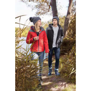A red puffer jacket worn by a woman and a black puffer jacket worn by a man, both outdoors near trees.