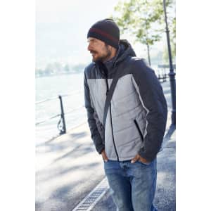 A men's puffer jacket in grey and dark grey, featuring a hood, with a casual beanie and denim jeans.