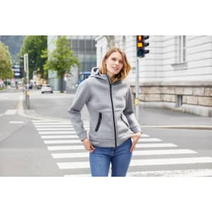 A grey ladies hooded jacket with a zip front and pockets, modelled by a woman in a casual outdoor setting.
