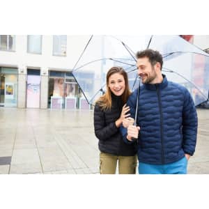 A modern padded jacket in navy, worn by a smiling man and woman under a clear umbrella in a city setting.