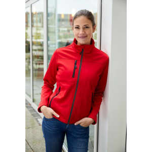 A red ladies softshell jacket with a high collar and zippered pockets, featuring a branding logo.