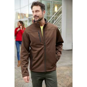 A men's softshell jacket in brown, featuring a zippered chest pocket and a high collar, worn by a man outdoors.