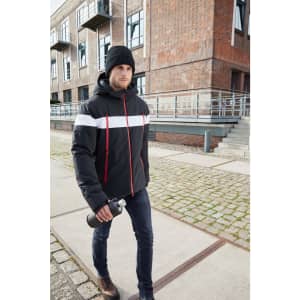 A man in a black winter sports jacket with white and red stripes, wearing a beanie, walking with a drink bottle outdoors.