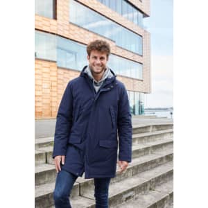 A men's business parka in navy blue, featuring a hood and pockets, worn by a smiling man on outdoor steps.
