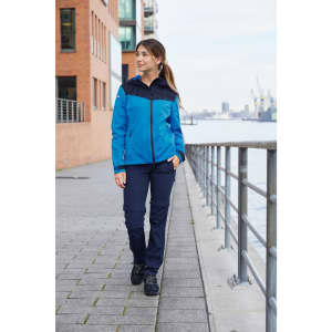 A blue and navy ladies' all-weather jacket worn by a woman walking along a waterfront promenade.