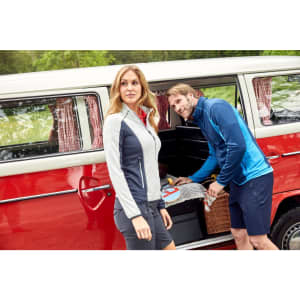 A pair of men's trekking shorts in navy blue, styled with a light grey and red zip-up jacket beside a vintage van.