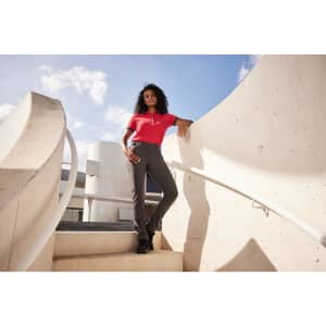 A woman stands on a staircase wearing grey slacks and a red top, set against a modern architectural background.