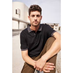 A black polo shirt with grey accents, worn by a man sitting outdoors, showcasing a casual look.