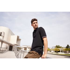 A black men's polo shirt worn by a man, set against an urban backdrop with contemporary architecture.
