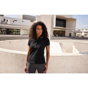 A black ladies polo shirt featuring a collar and a logo, modelled by a woman in an outdoor setting.