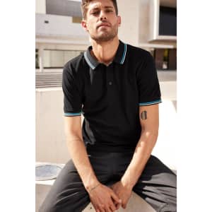 A black men’s polo shirt with turquoise accents, featuring a logo, worn by a man sitting outdoors.
