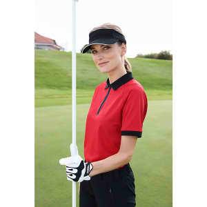 A model in a red polo shirt with black accents, holding a golf flag, wearing a visor and golf glove.