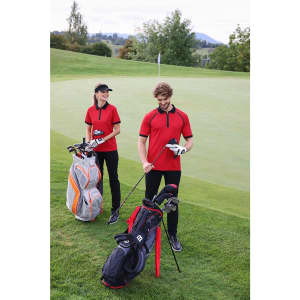 A red zip-polo shirt is worn by a man and woman on a golf course, with golf bags beside them.