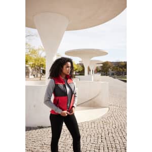 A woman wearing a red and grey fleece vest stands outdoors near modern architectural features.