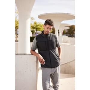 A men's fleece vest in black, featuring a zip front and a logo, worn by a model in an outdoor setting.