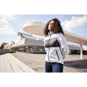 A grey and black ladies fleece jacket with a front zip and pockets, worn by a model outdoors.