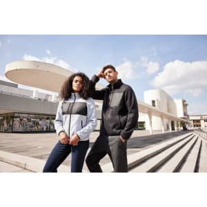 A fleece jacket in light blue and black, worn by two models outside a modern building, featuring a logo.