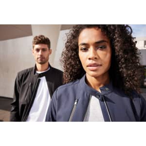 A navy ladies softshell jacket featured on a model with curly hair, alongside a male model in a black jacket.
