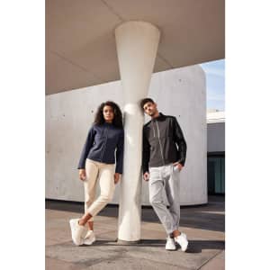 A navy blue ladies softshell jacket is worn by a woman, while a man models a black jacket. Both pair with light-tone pants.