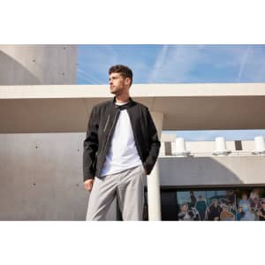 A mens softshell jacket in black, worn over a white shirt, displayed against a modern architectural background.