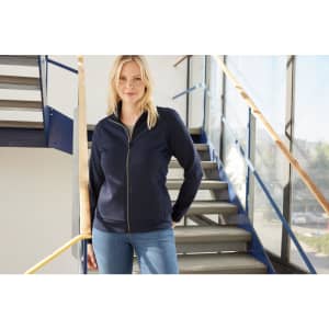 A navy ladies jacket with a zip front, worn by a model standing on a staircase. The jacket has a logo.