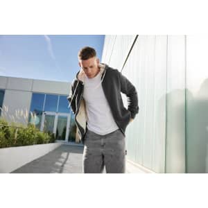 A model wears a grey doubleface jacket with a contrasting hood, paired with light grey pants, against a modern building backdrop.