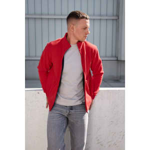 A man in a red bonded fleece jacket and grey t-shirt stands against a minimalist background. The jacket features a logo.